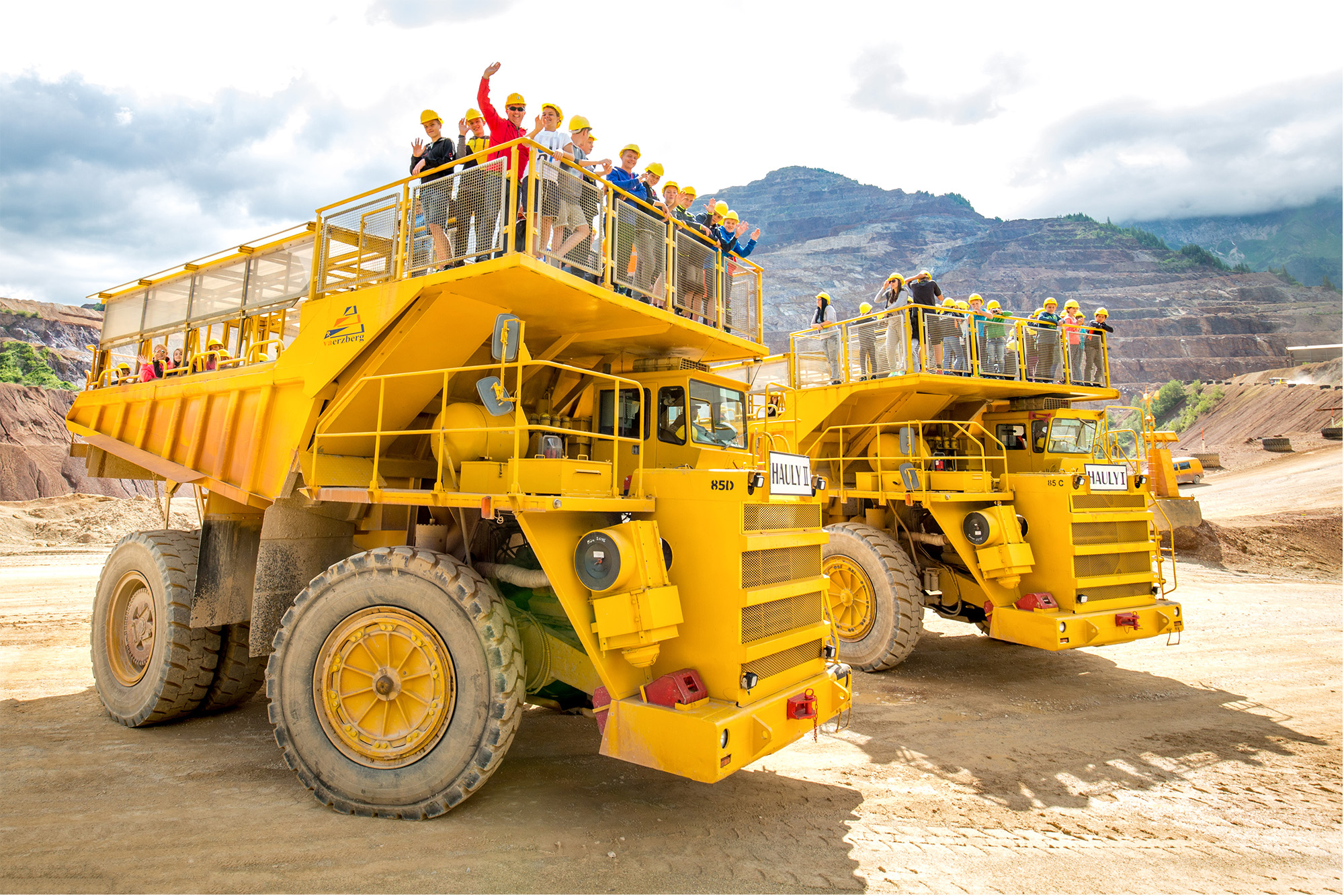 Gelbe Bergbau-Fahrzeuge mit Touristen in der Bergbaulandschaft, Link zur Erlebniswelt Abenteuer.